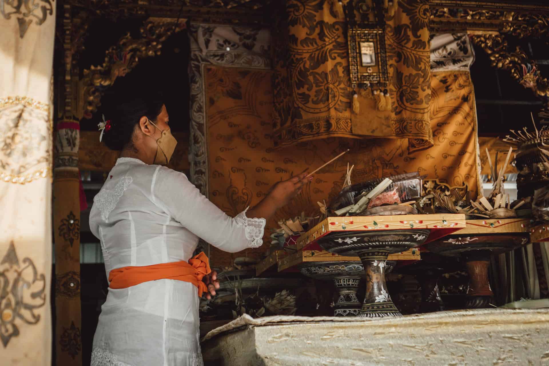 A woman wearing a white robe is standing in front of a shrine, showcasing cultural nuances.