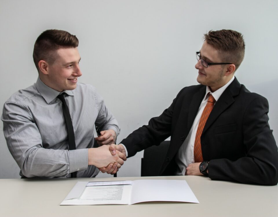 Two men shaking hands while sitting at a desk, discussing export partnerships with developing distributors.