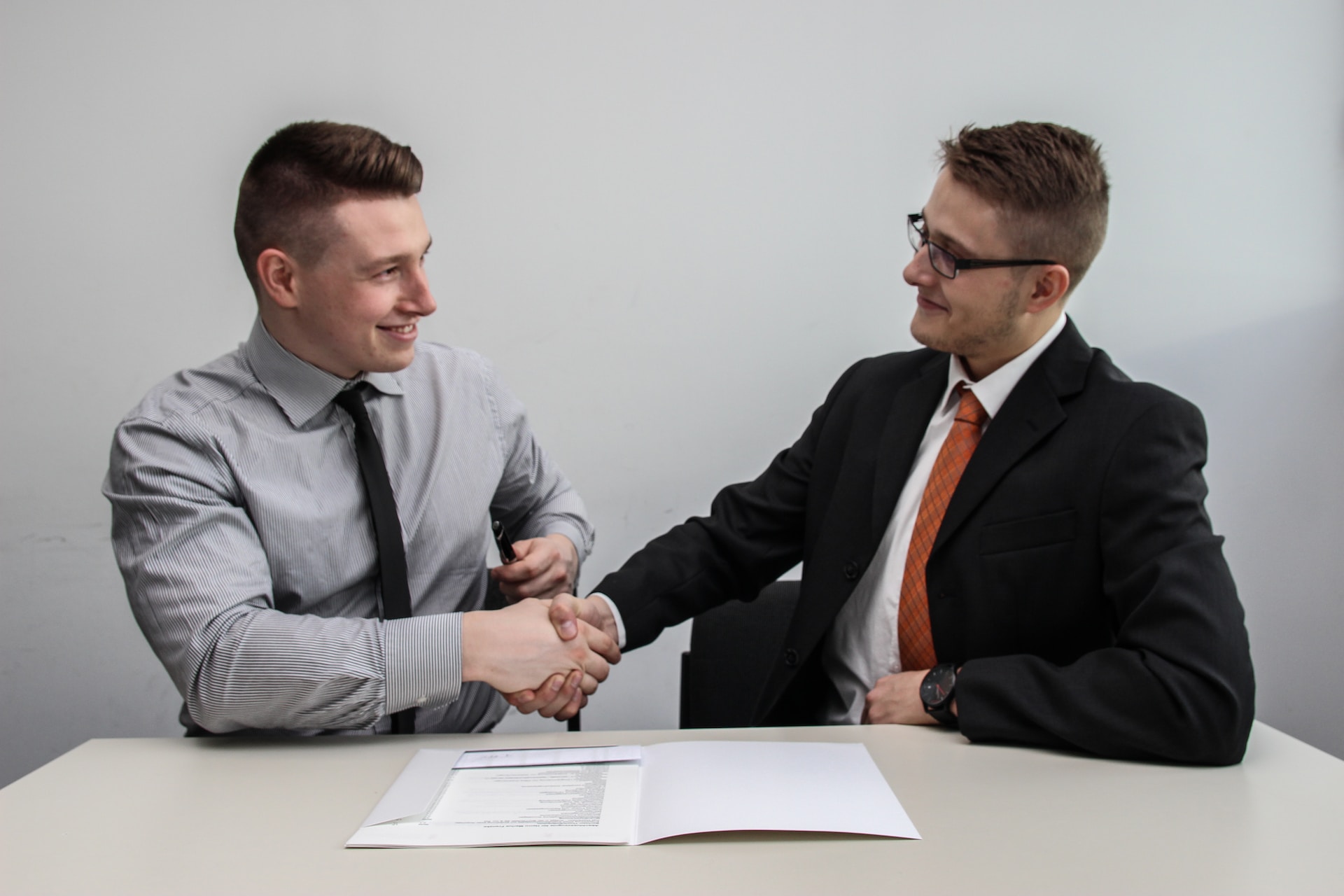 Two men shaking hands while sitting at a desk, discussing export partnerships with developing distributors.