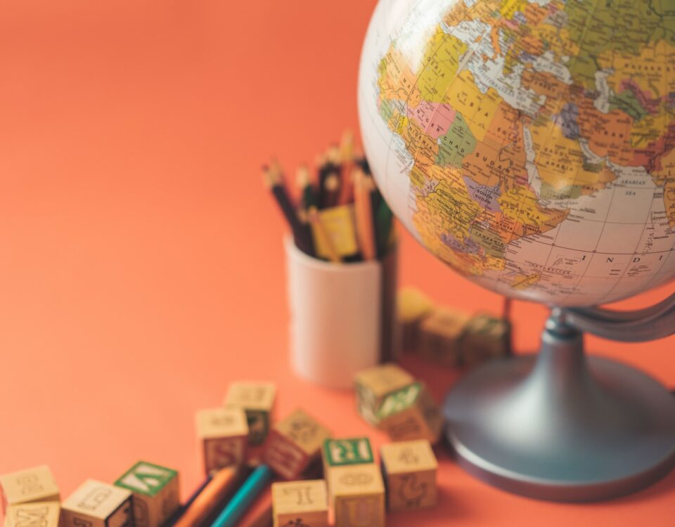 An orange background with a globe representing international trade and globalization, adorned with wooden blocks and pencils.