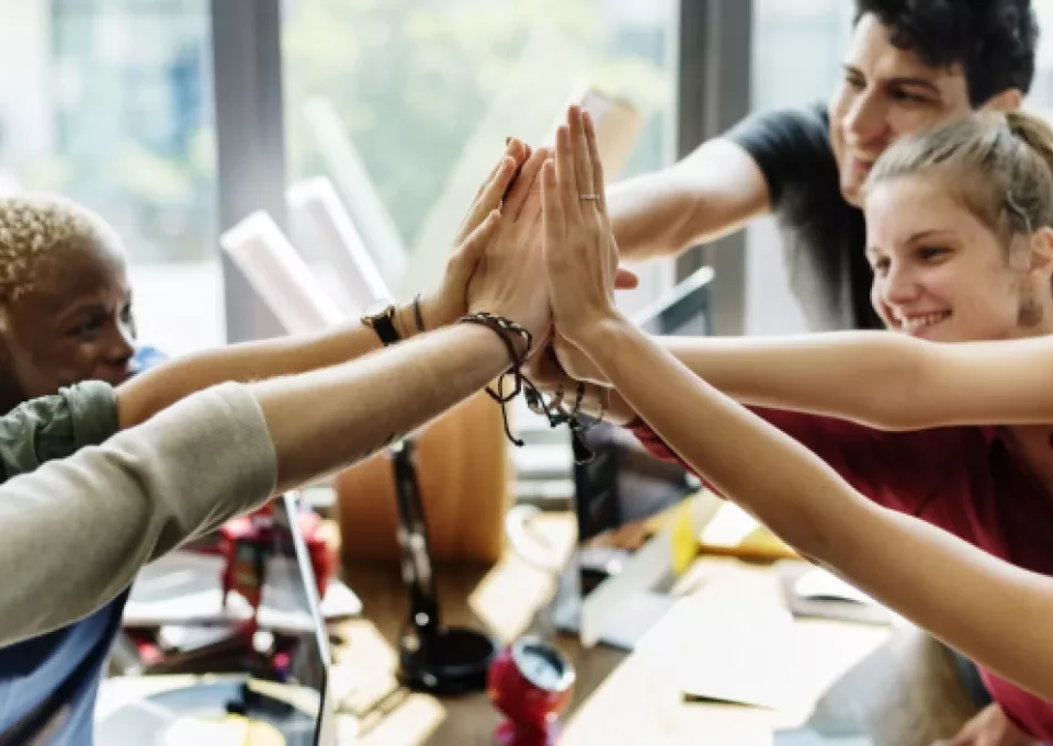 A diverse group of people exchanging high fives in an office, showcasing cultural differences and illustrating the importance of international trade practices.