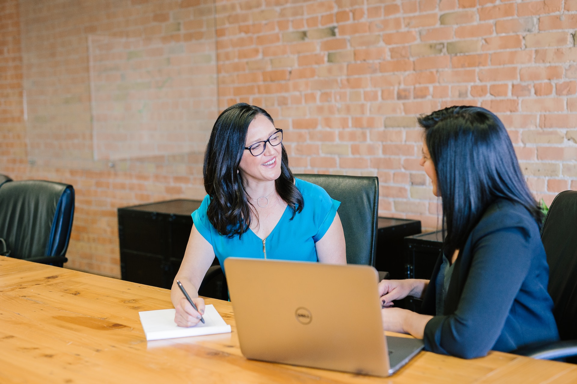 Two women engaged in cross-cultural negotiation strategies, attentively sitting at a conference table with laptops.