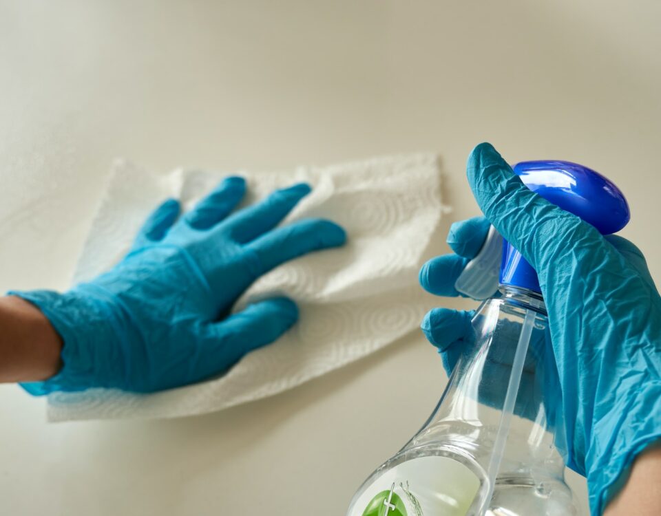 An individual in blue gloves diligently cleansing a wall with a bottle of cleaner amidst the Covid-19 pandemic.