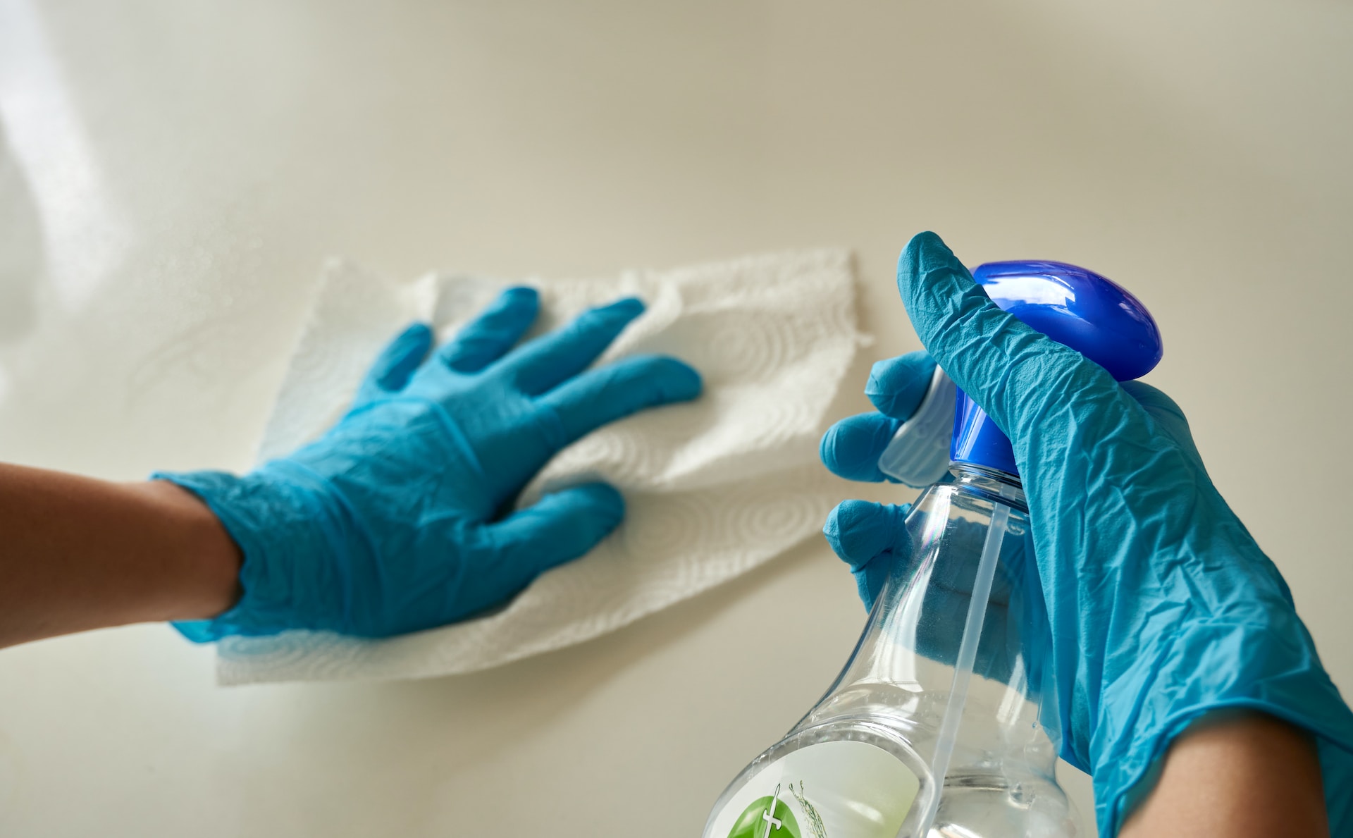 An individual in blue gloves diligently cleansing a wall with a bottle of cleaner amidst the Covid-19 pandemic.