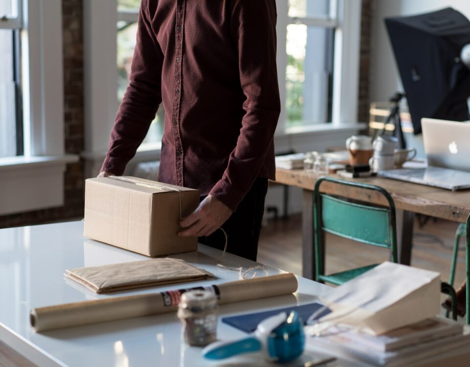 A man from a SME is holding a box in front of a desk, discussing export financing options.