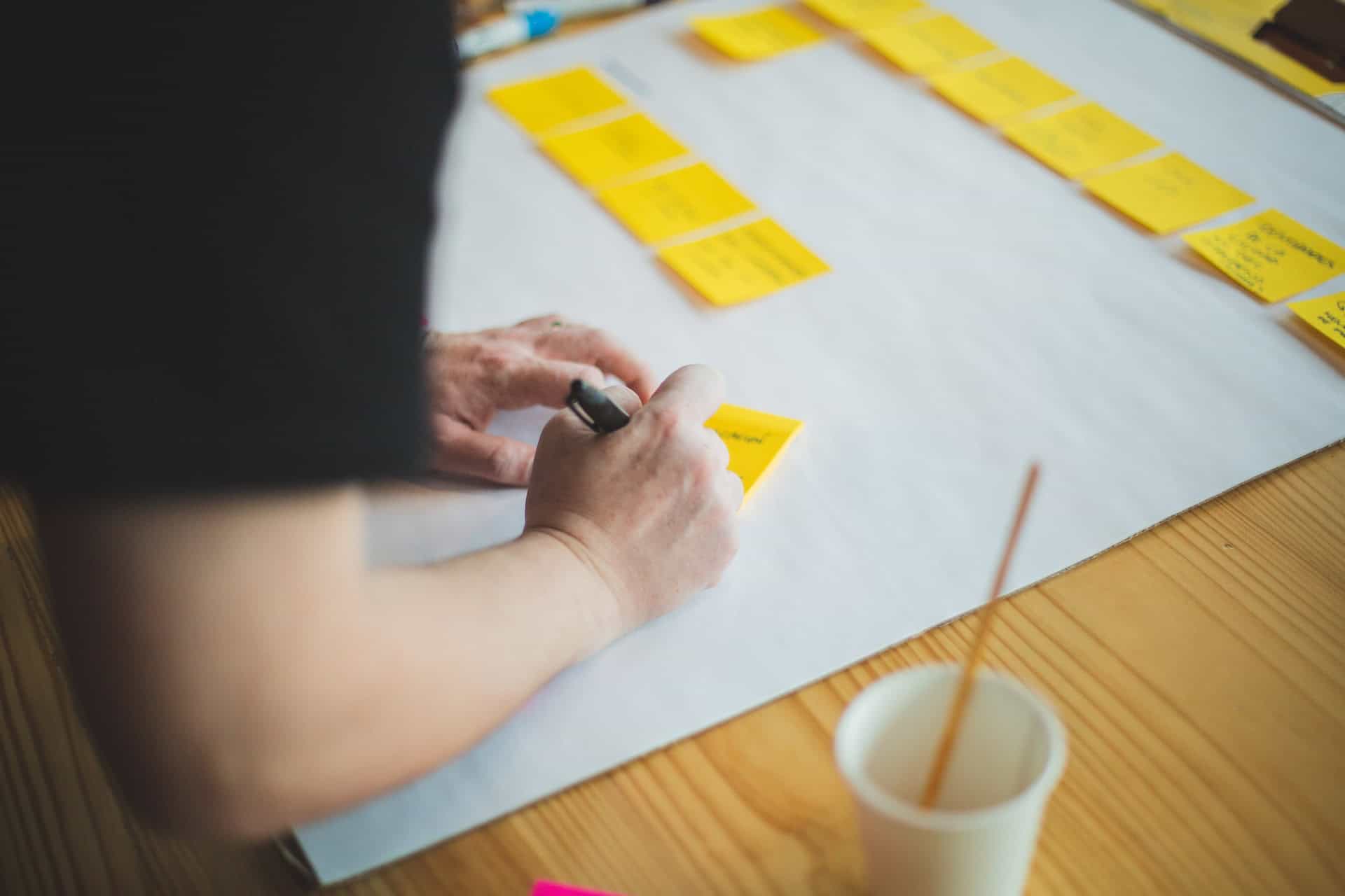 A person implementing market penetration strategies by writing on a piece of paper with yellow post it notes.