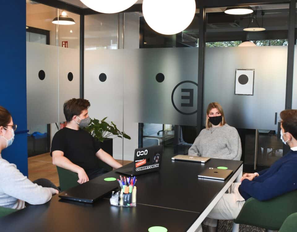 Amid the ongoing COVID-19 pandemic, a group of people is seated around a table in an office, discussing the effects of international trade.