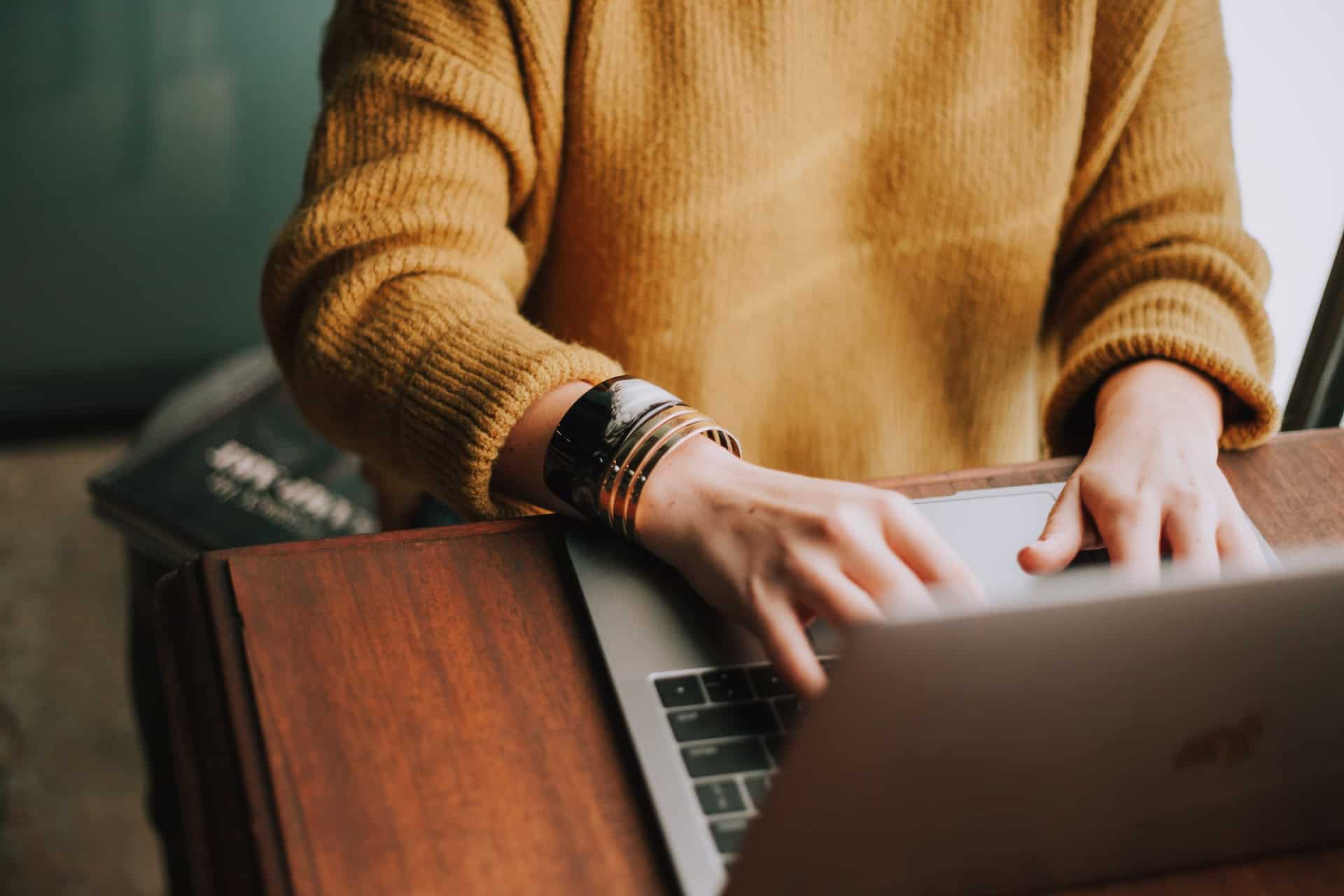 A woman in a yellow sweater immersed in cultural nuances while typing on a laptop during business negotiations.