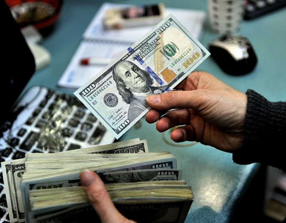 A person is holding a stack of money in front of a laptop, demonstrating currency management in cross-border payments.