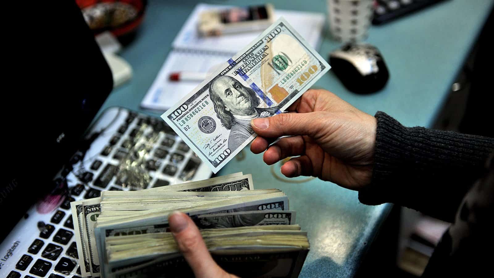 A person is holding a stack of money in front of a laptop, demonstrating currency management in cross-border payments.