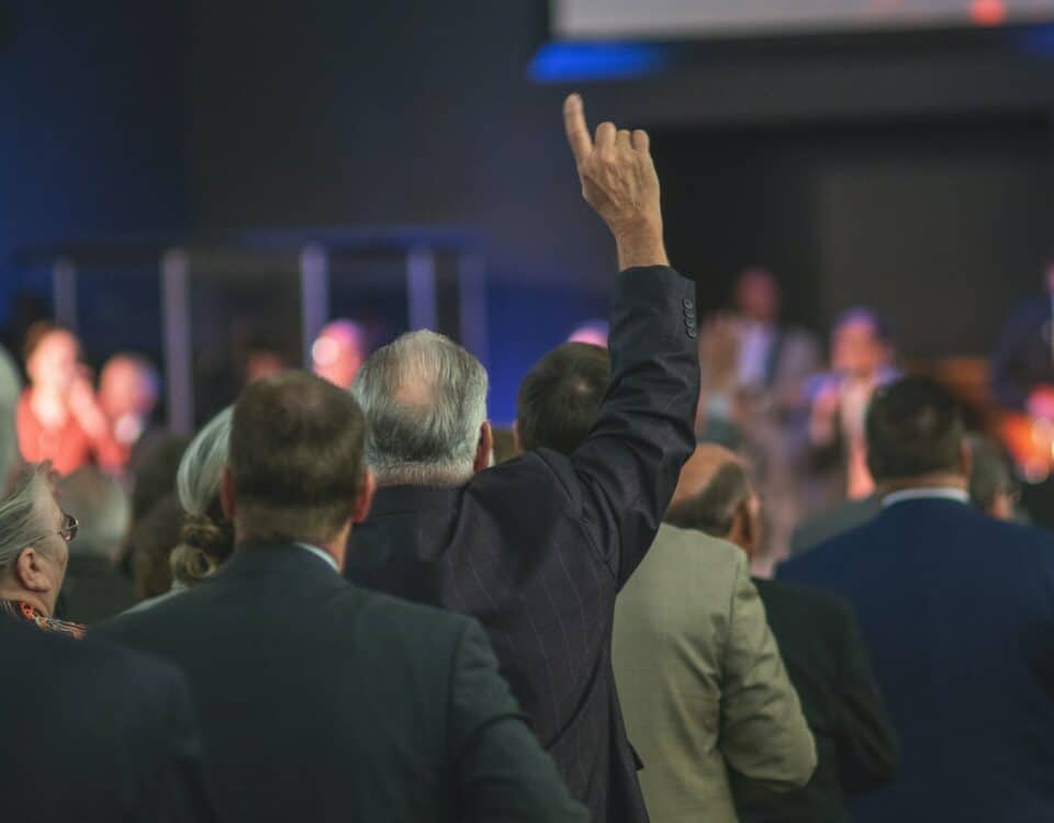 A man in a suit raises his hand in front of a crowd, symbolizing his influential role in international trade as a representative of the World Trade Organization.