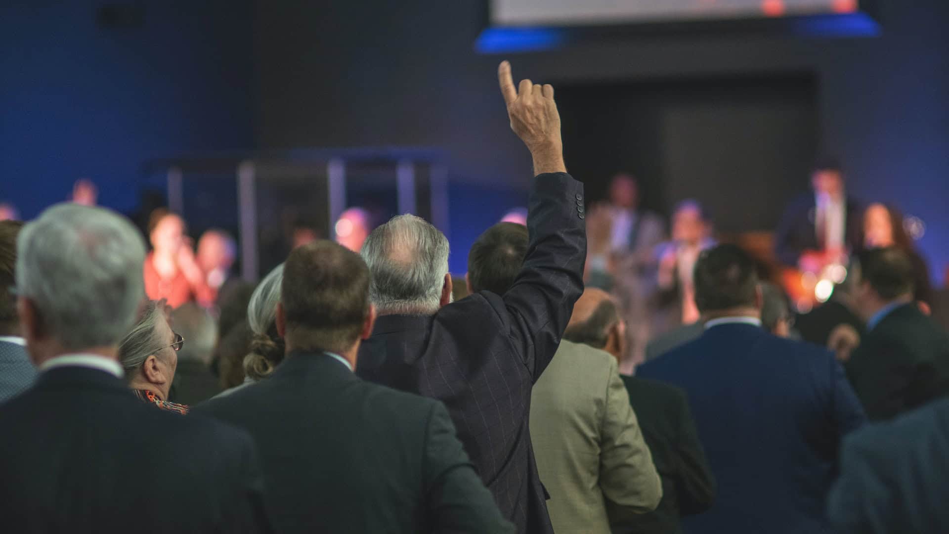 A man in a suit raises his hand in front of a crowd, symbolizing his influential role in international trade as a representative of the World Trade Organization.