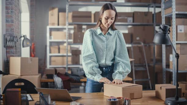 A robust woman is opening an export box in a developing warehouse.