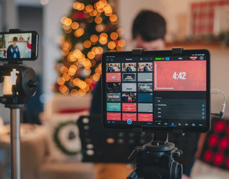 A socially responsible man is using a video camera to record a sustainable Christmas video in front of a Christmas tree.