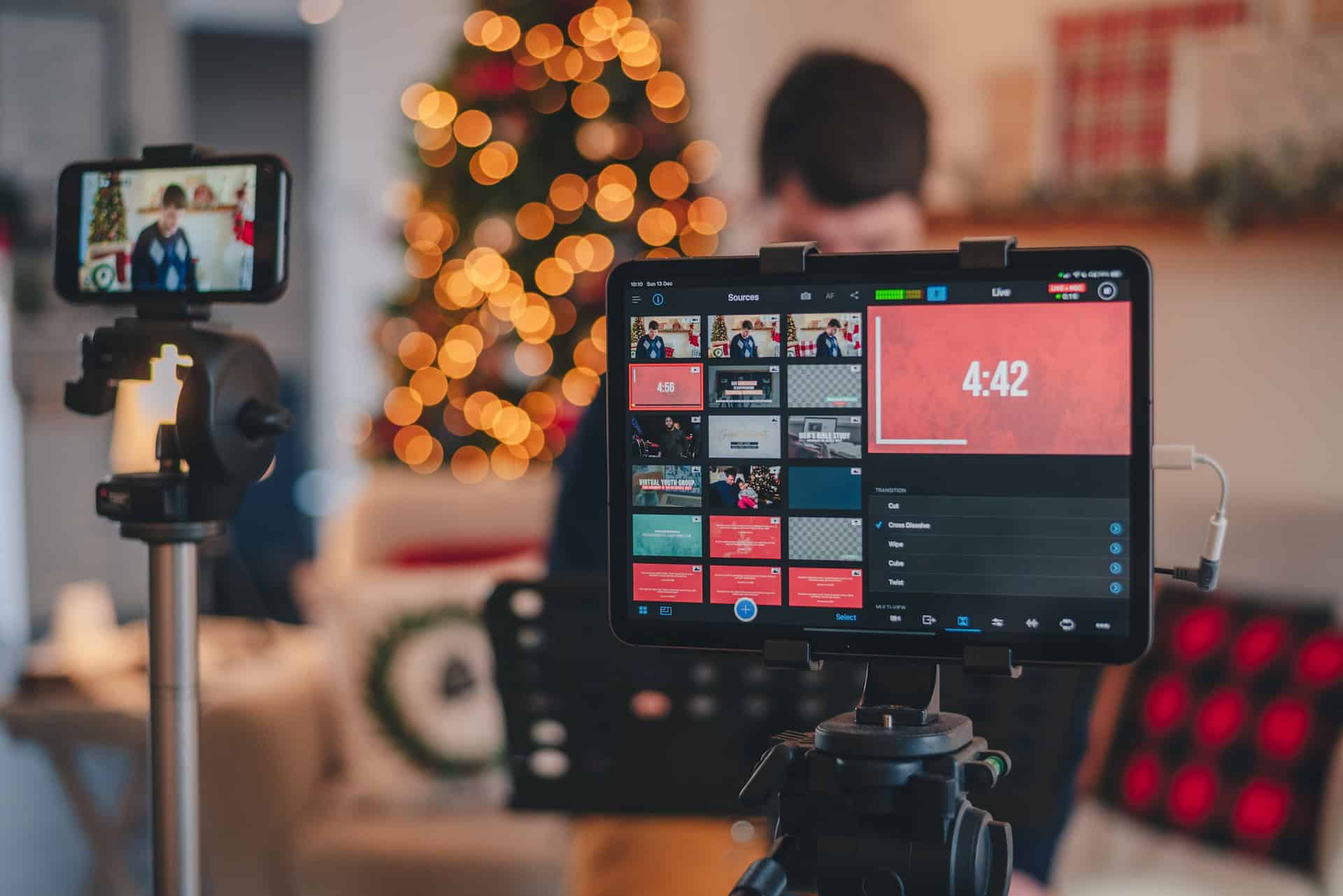 A socially responsible man is using a video camera to record a sustainable Christmas video in front of a Christmas tree.