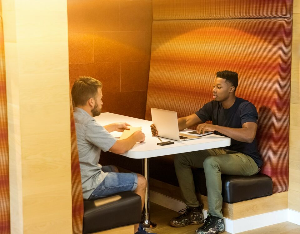 Two men engaged in international business sitting at a table with laptops, discussing trade agreements.