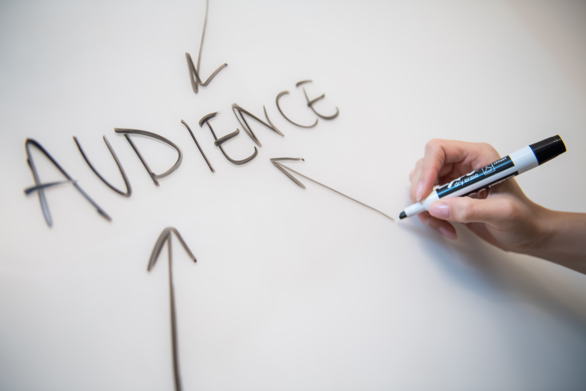 A person writing the word "audience" on a whiteboard during a marketing meeting, emphasizing the importance of cultural sensitivity in advertising.