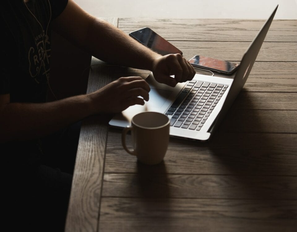 A man sitting at a table with a laptop and a cup of coffee, emphasizing sustainability practices in corporate social responsibility.