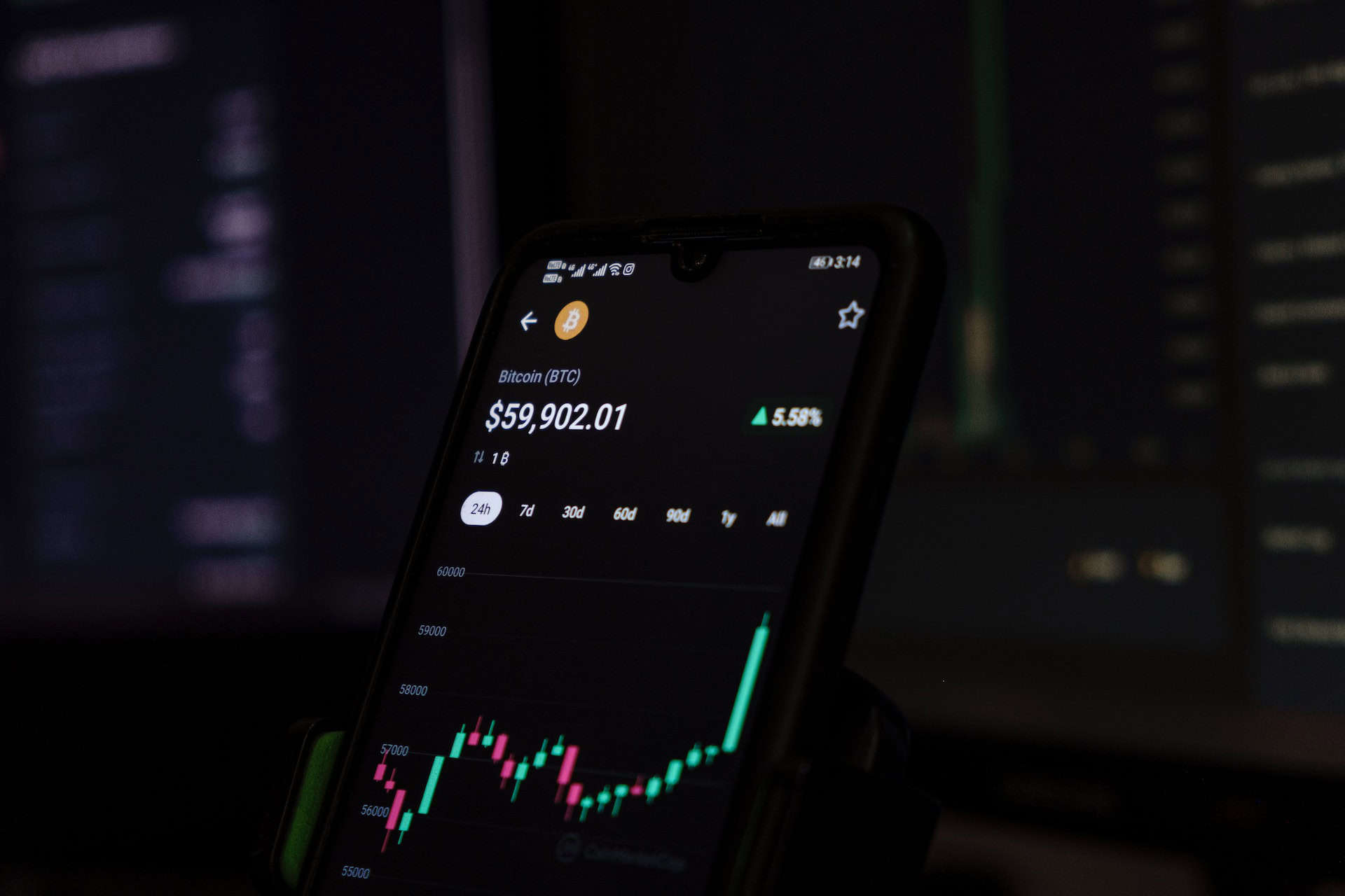 A person is holding a cell phone in front of a computer screen to analyze trade finance options or manage risks.