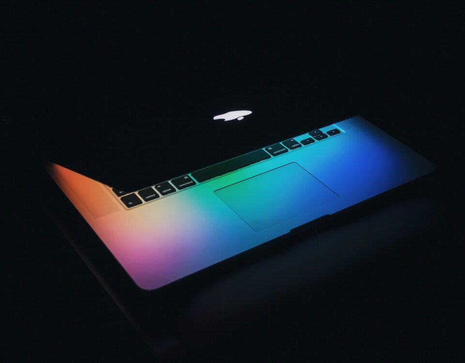 A technologically advanced macbook pro showcasing export success, highlighted by its rainbow colored appearance in the dark.