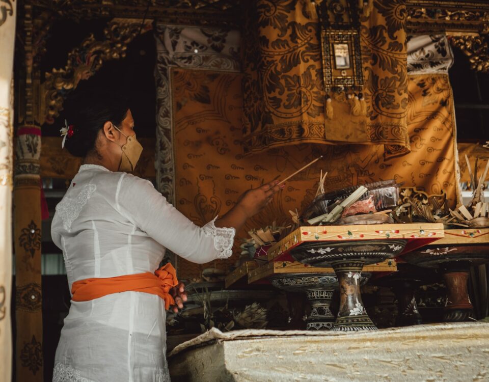 A woman wearing a white robe is standing in front of a shrine, showcasing cultural nuances.