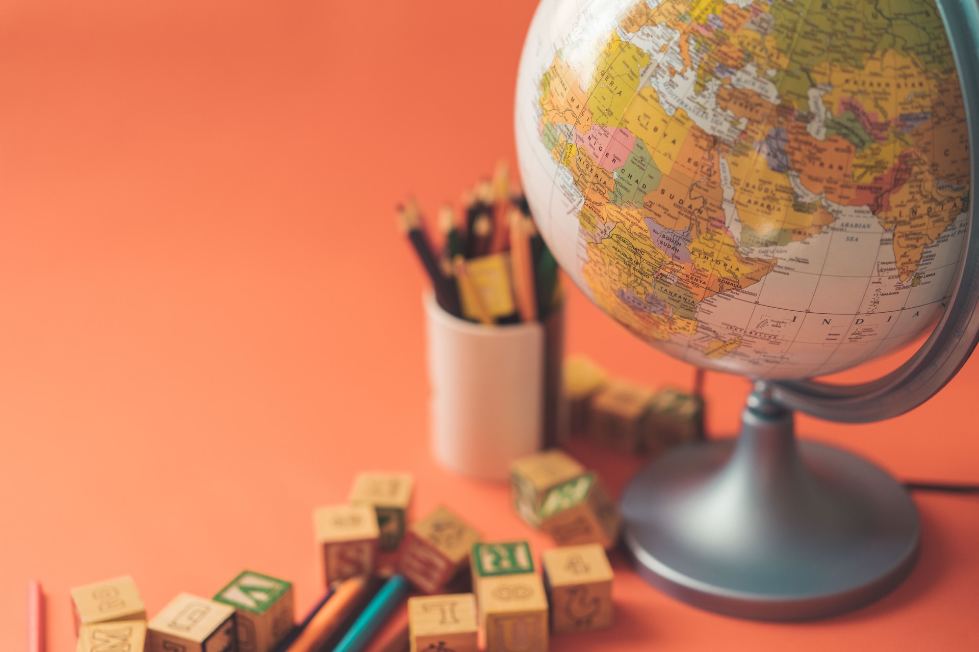 An orange background with a globe representing international trade and globalization, adorned with wooden blocks and pencils.