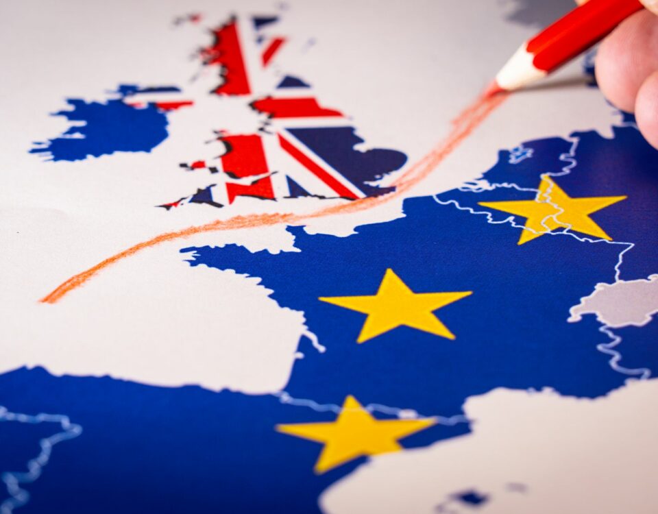 A person is drawing a red line on a map with British and European flags, symbolizing the impact of Brexit on international trade.