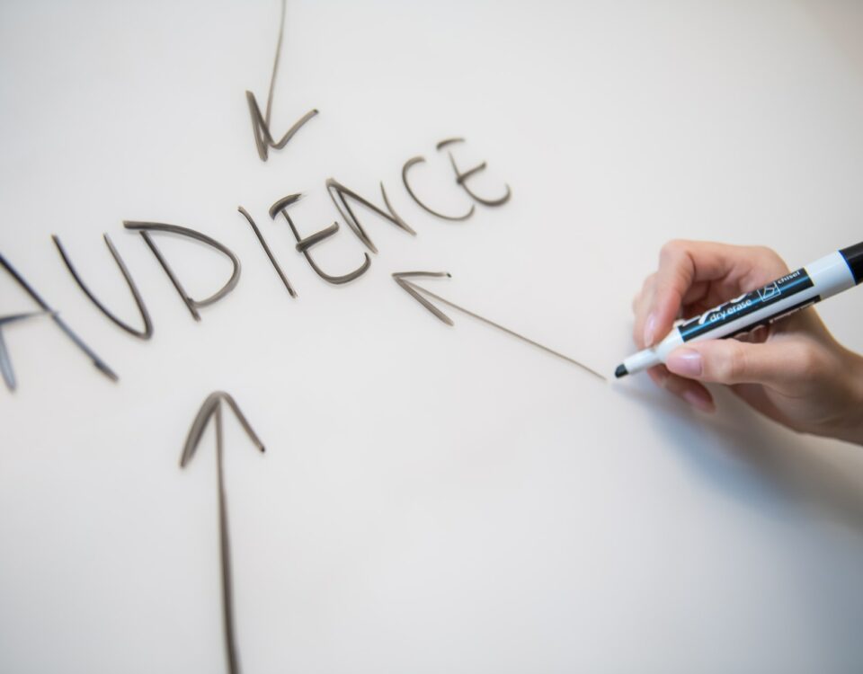 A person writing the word "audience" on a whiteboard during a marketing meeting, emphasizing the importance of cultural sensitivity in advertising.