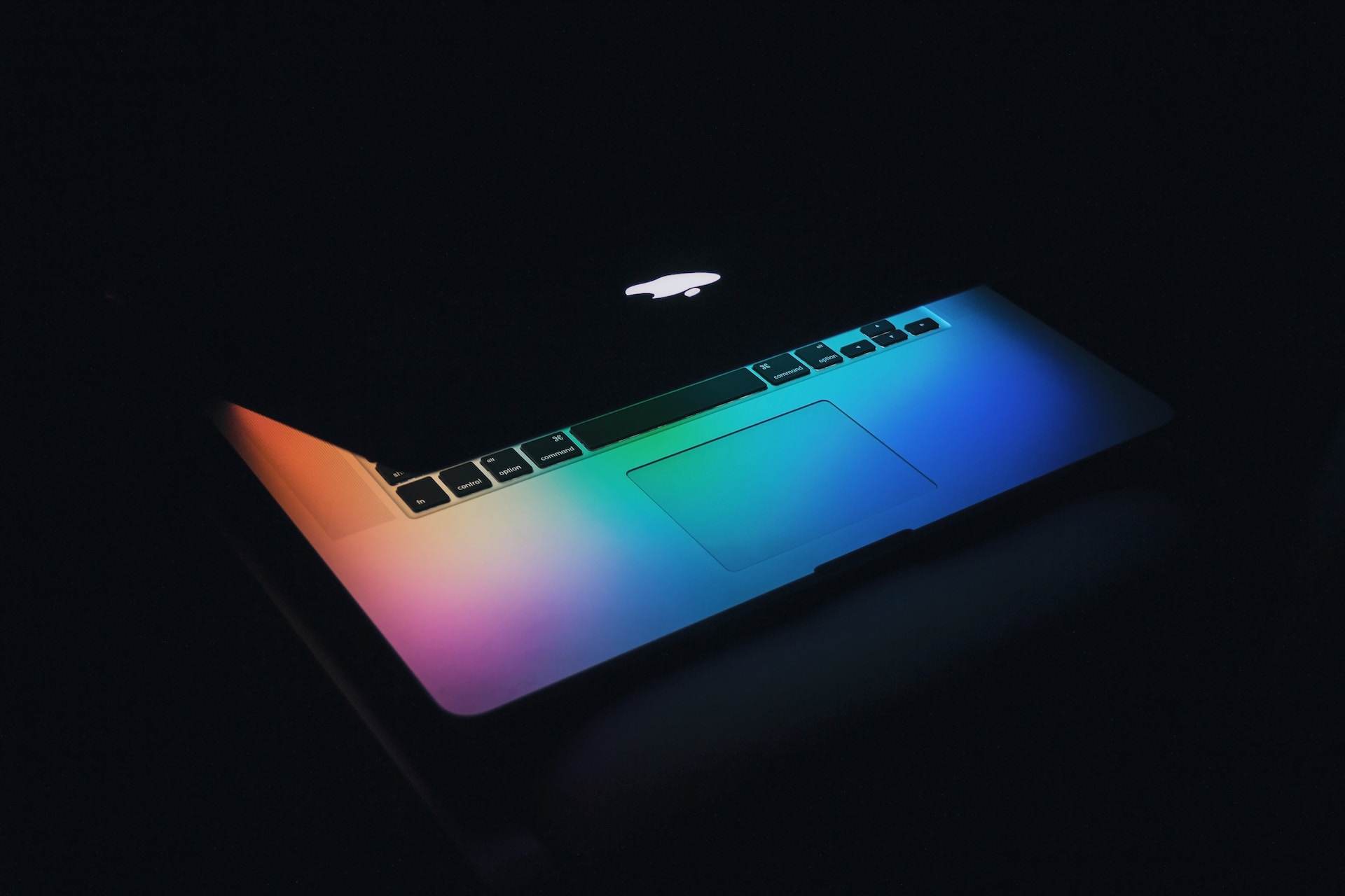 A technologically advanced macbook pro showcasing export success, highlighted by its rainbow colored appearance in the dark.